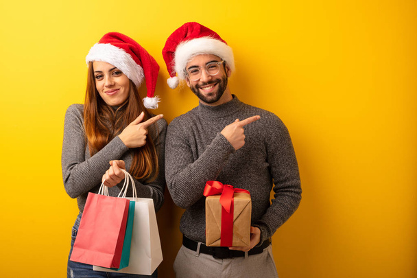Couple ou amis tenant des cadeaux et des sacs à provisions souriant et pointant vers le côté
 - Photo, image
