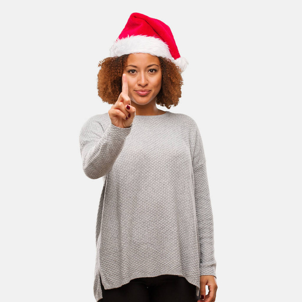 Young black woman wearing a santa hat showing number one - Photo, Image