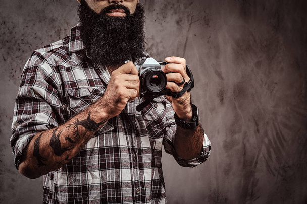 Immagine ritagliata di un maschio barbuto tatuato che indossa una camicia a scacchi con una fotocamera
. - Foto, immagini