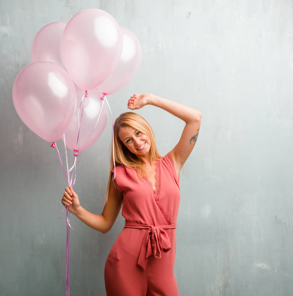 Elegante joven rubia sosteniendo globos rosados contra una pared
. - Foto, Imagen