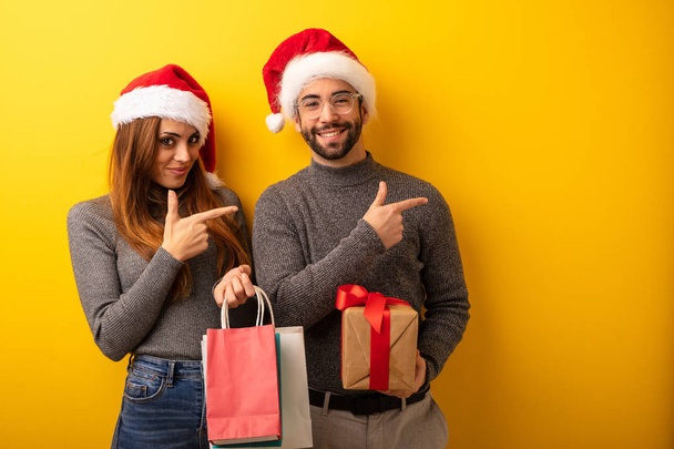 Couple or friends holding gifts and shopping bags pointing to the side with finger - Photo, Image