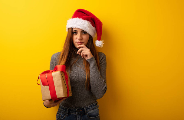 Young pretty woman holding gift doubting and confused - Photo, Image