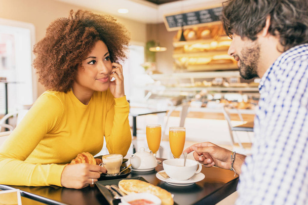 Mladý pár má na snídani v kavárně, pijí čaj a káva a pomerančový džus. Při pohledu na sebe. - Fotografie, Obrázek