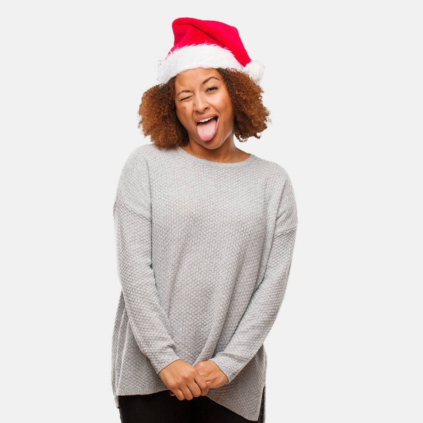 Young black woman wearing a santa hat funnny and friendly showing tongue - Photo, Image