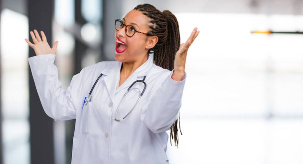 Προσωπογραφία γυναίκας νεαρό μαύρο γιατρό ουρλιάζοντας ευτυχισμένος, έκπληκτος από μια προσφορά ή μια προαγωγή, Πήδημα από συμμορία, άλμα και περήφανο - Φωτογραφία, εικόνα