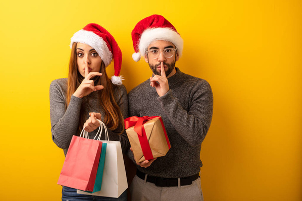 Couple or friends holding gifts and shopping bags keeping a secret or asking for silence - Photo, Image