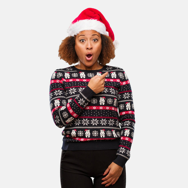 Jeune femme noire dans un pull de Noël à la mode avec une impression pointant vers le côté
 - Photo, image