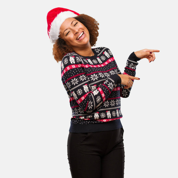Mujer negra joven en un suéter de Navidad de moda con estampado apuntando hacia un lado con el dedo
 - Foto, imagen