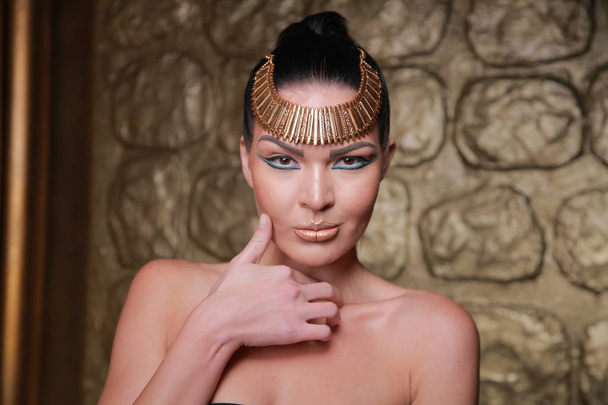 Kaunis ruskeaverikkö poseeraamassa. Egypti Style Rich Luxury nainen koruja kultainen tausta
. - Valokuva, kuva
