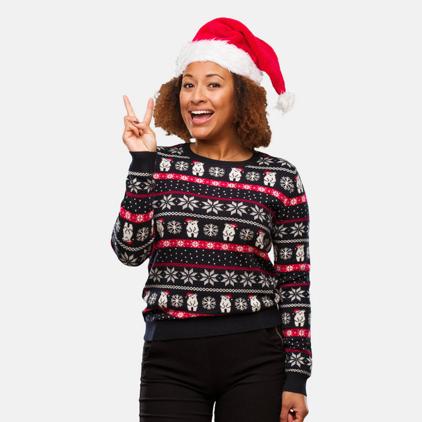 Νεαρή μαύρη γυναίκα σε ένα καθιερώνον τη μόδα Χριστούγεννα πουλόβερ με print διασκεδαστική και ευτυχής να κάνει μια χειρονομία της νίκης - Φωτογραφία, εικόνα
