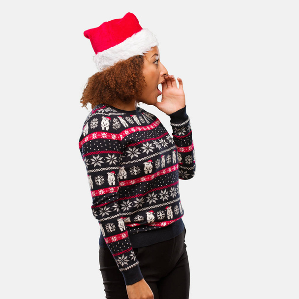 Jeune femme noire dans un pull de Noël à la mode avec impression chuchotant commérages sous-ton
 - Photo, image