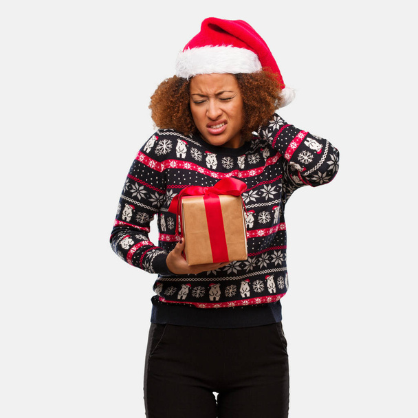 Young black woman holding a gift in christmas day suffering neck pain - Foto, Bild