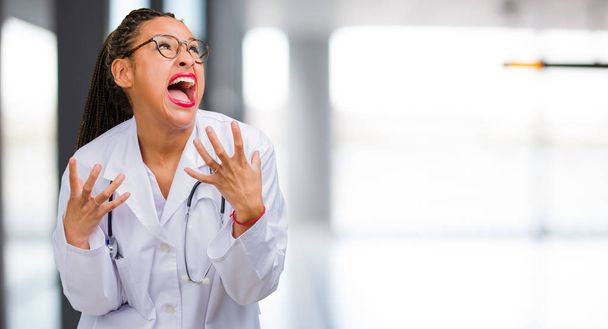 Portrét ženy mladý černý doktor velmi naštvaný a rozrušený, velmi napjatá, křičí zběsile, negativní a blázen - Fotografie, Obrázek