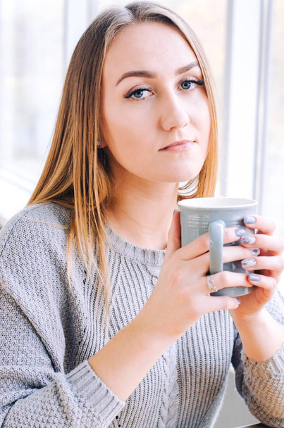 Красива дівчина в сірому светрі з сірою чашкою кави або чаю
. - Фото, зображення