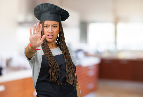 Portrait of a young black baker woman serious and determined, putting hand in front, stop gesture, deny concept - Photo, Image