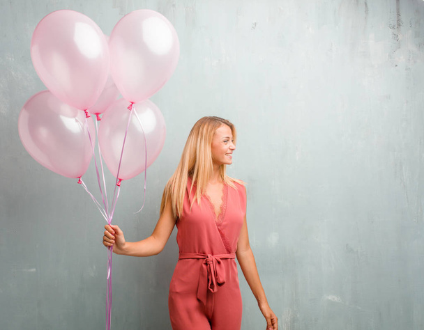 Elegante giovane donna bionda che tiene palloncini rosa contro un muro
. - Foto, immagini