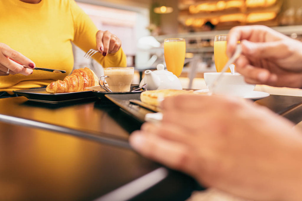 Paar met een ontbijt in het café, ze eet een croissant, beide zijn het drinken van een jus d'orange. - Foto, afbeelding