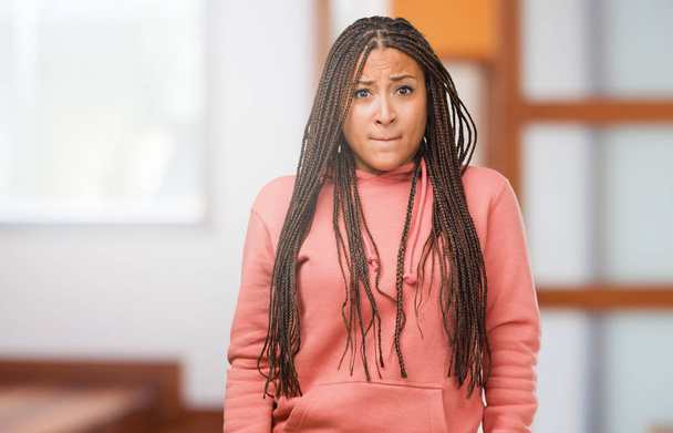 Portrait of a young black woman wearing braids doubting and confused, thinking of an idea or worried about something - Photo, Image