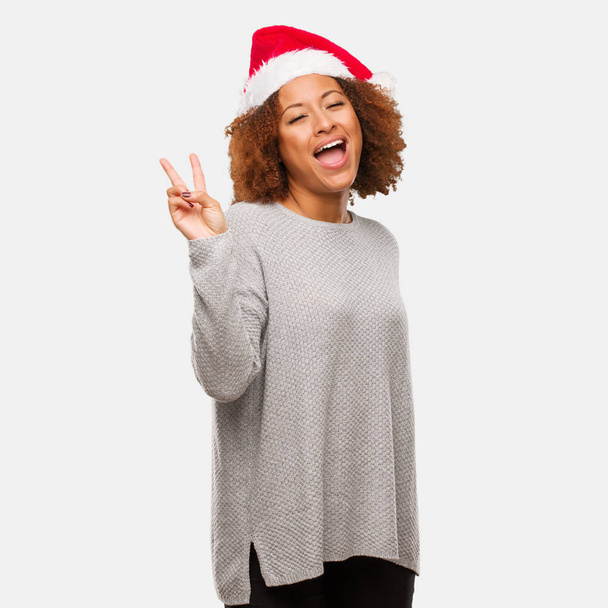 Fiatal fekete nő, fárasztó egy santa kalap csinál egy gesztus, a győzelmet - Fotó, kép