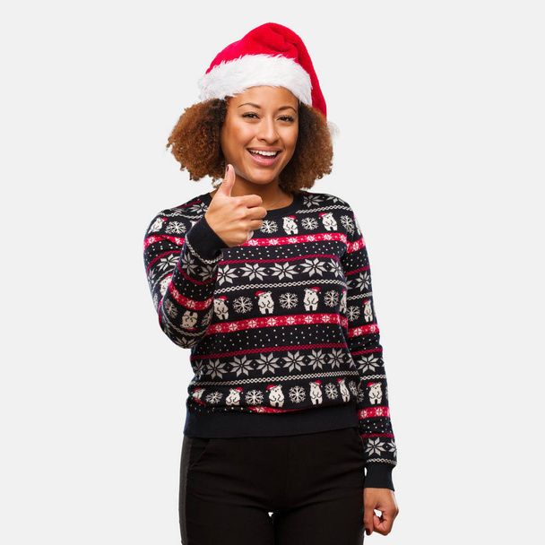 Jovem mulher negra em uma camisola de Natal na moda com impressão sorrindo e levantando o polegar
 - Foto, Imagem