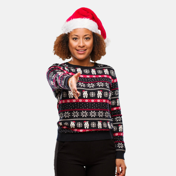 誰かを迎えるために印刷を差し伸べると流行のクリスマス セーターの若い黒人女性 - 写真・画像