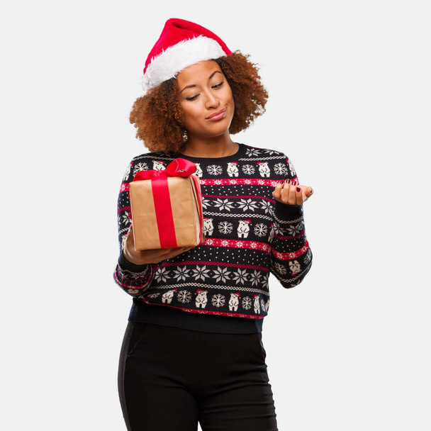 Νεαρή μαύρη γυναίκα, κρατώντας ένα δώρο για την ημέρα των Χριστουγέννων, σύγχυση και αμφίβολο - Φωτογραφία, εικόνα