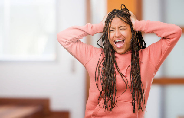 Portrait of a young black woman wearing braids crazy and desperate, screaming out of control, funny lunatic expressing freedom and wild - Photo, Image