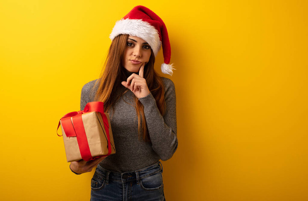 Young pretty woman holding gift doubting and confused - Photo, Image