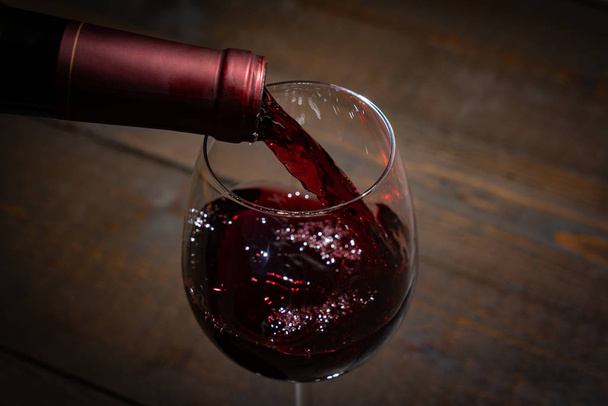 Красное вино, наливаемое в бокал из бутылки
 - Фото, изображение