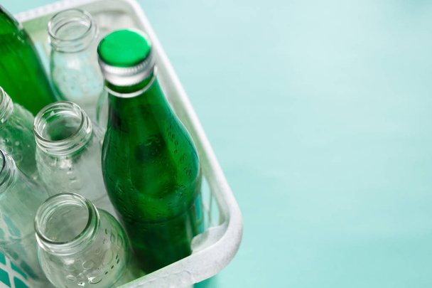 different glass bottle wastes ready for recycling in white basket on green background. Social responsibility, ecology care, recycling at home concept - Photo, Image