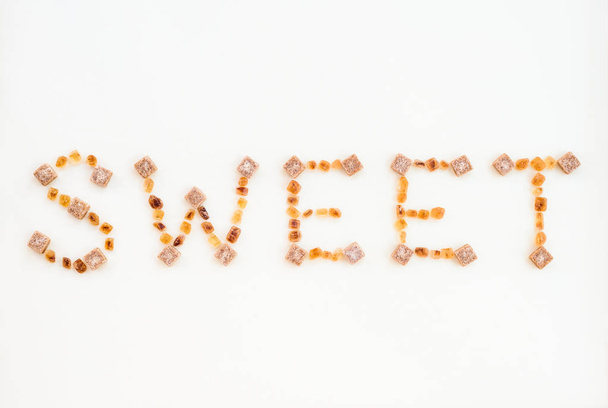 The word SWEET written with brown sugar pieces, on white background. - Photo, Image