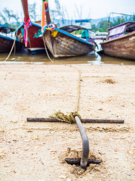 Rezavá kotva na písčité pláži s tradiční dlouhou lodí na moře v Thajsku svislý styl. - Fotografie, Obrázek