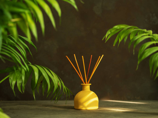 Aroma reed diffuser with rattan sticks with palm leaves on dark background - Photo, Image