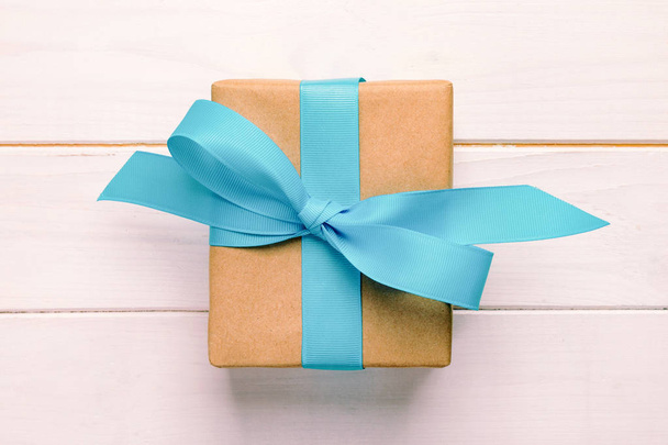 Подарочная коробка с голубым бантом над белым деревянным столом с копировальным местом. винтажный, тонированный вид сверху
. - Фото, изображение