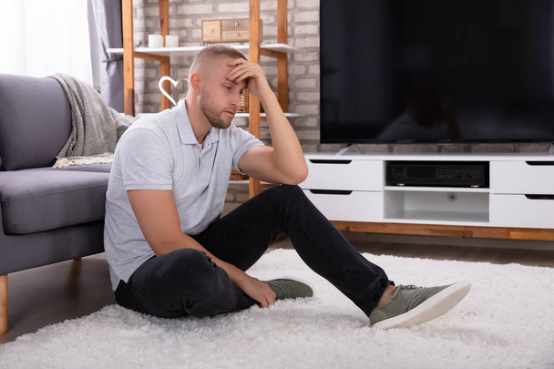 Side View Of A Upset Young Man Sitting Near Sofa - Foto, Bild