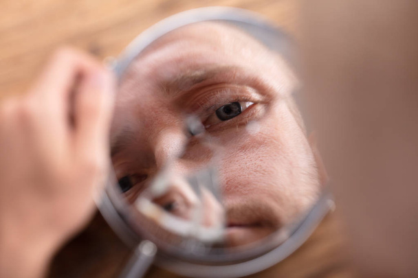 Close-up Of A Man's Face In Broken Mirror Over Wooden Desk - Foto, Bild