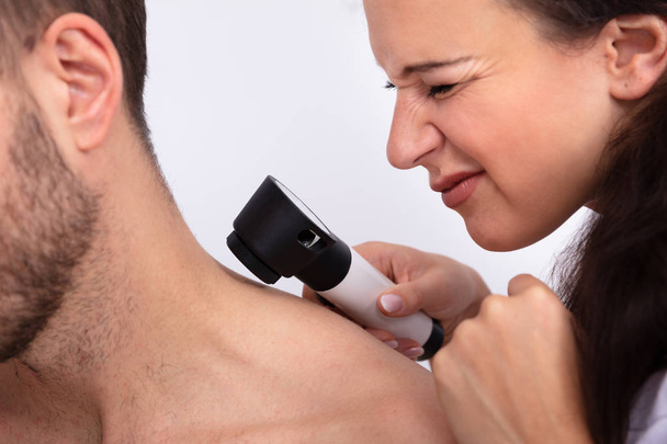 Крупним планом молода жінка лікар перевіряє шкіру на шиї людини з дерматоскопом
 - Фото, зображення
