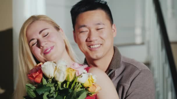 Happy young couple with a bouquet of flowers. Smiling, looking at the camera. Asian man and Caucasian woman - Imágenes, Vídeo