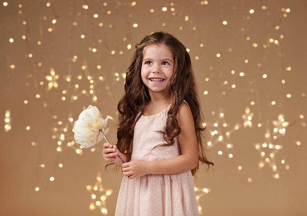 meisje kind is in Kerstverlichting, gele achtergrond, roze jurk - Foto, afbeelding