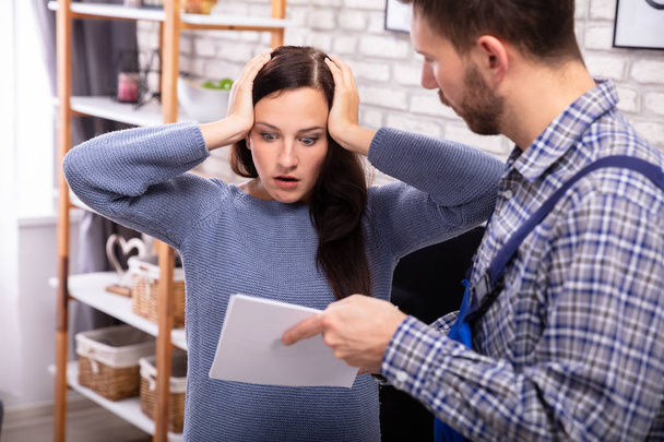 Shocked Woman Looking At Invoice Shown By Male Technician - Φωτογραφία, εικόνα