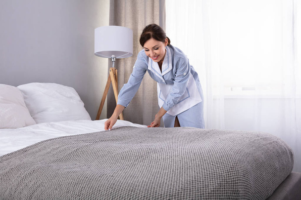 Smiling Female Housekeeper Making Bed In Hotel Room - 写真・画像
