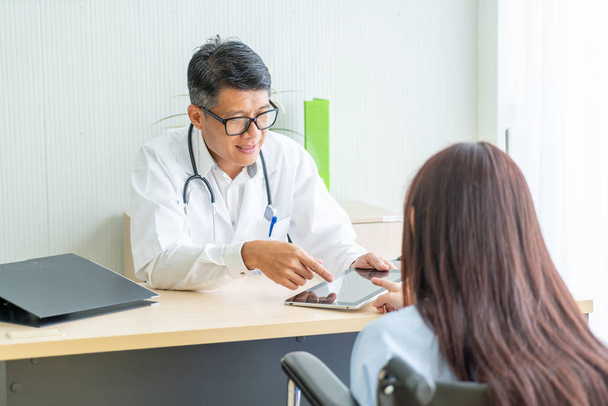 Asiatique médecin et patient sont consultation et discuter de quelque chose tout en étant assis à la table
 - Photo, image