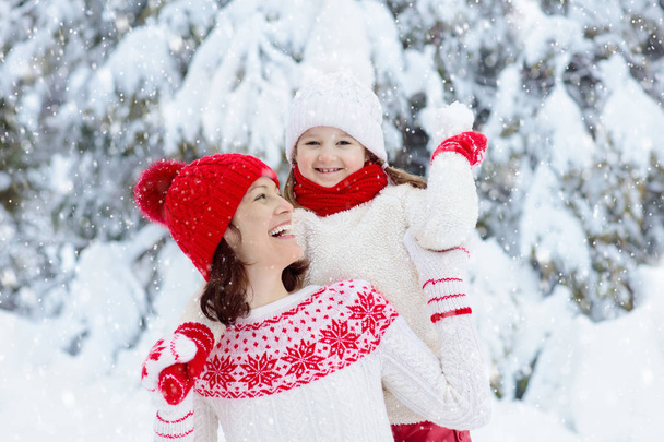 Mother and child in knitted winter hats play in snow on family Christmas vacation. Handmade wool hat and scarf for mom and kid. Knitting for kids. Knit outerwear. Woman and little girl in snowy park. - Photo, image