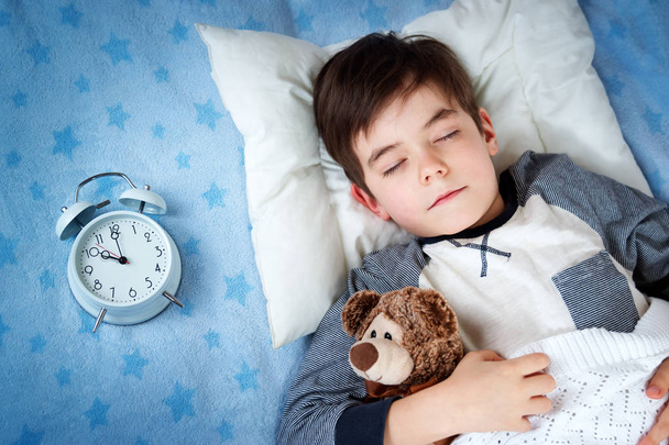 six years old child sleeping in bed with alarm clock - Foto, afbeelding