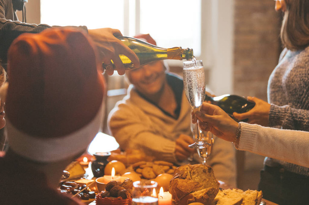 Christmas celebration with champagne - group of friends drinking and toasting together - a hand with bottle pouring sparkling wine in a glass (flute) - Zdjęcie, obraz