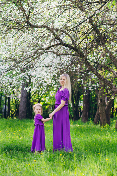 Young beautiful woman with a little daughter walking through the blooming Apple orchard. The concept of family rest and love. Toning. - Φωτογραφία, εικόνα