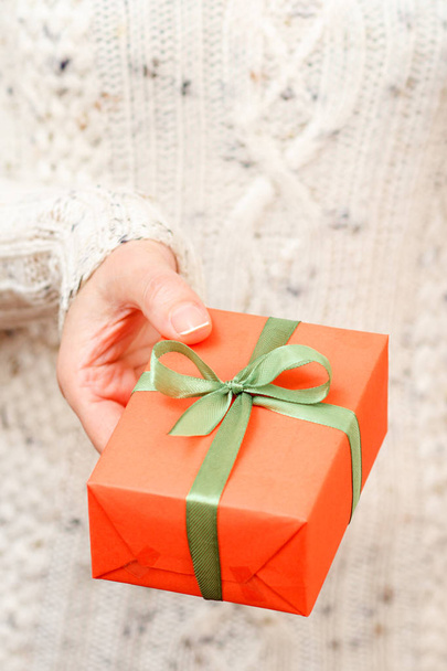 Woman holding a gift box tied with a green ribbon in her hand. Shallow depth of field, Selective focus on the box. Concept of giving a gift on holiday or birthday. - Foto, Imagem