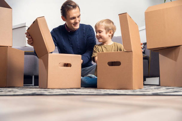 Photo of man and boy sitting on floor among cardboard boxes - Foto, immagini