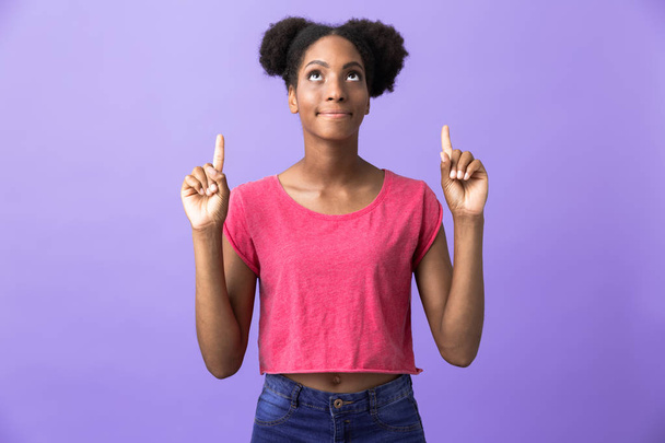 Photo of teen african american woman pointing fingers upward at copyspace isolated over violet background - Fotó, kép