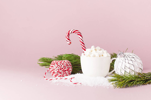 Christmas New Year drink, white mug with marshmallows and Candy Cane pine branches ball in the snow on pink background Flat Lay copy space. Winter traditional drink food Festive decor celebration Xmas - Photo, Image
